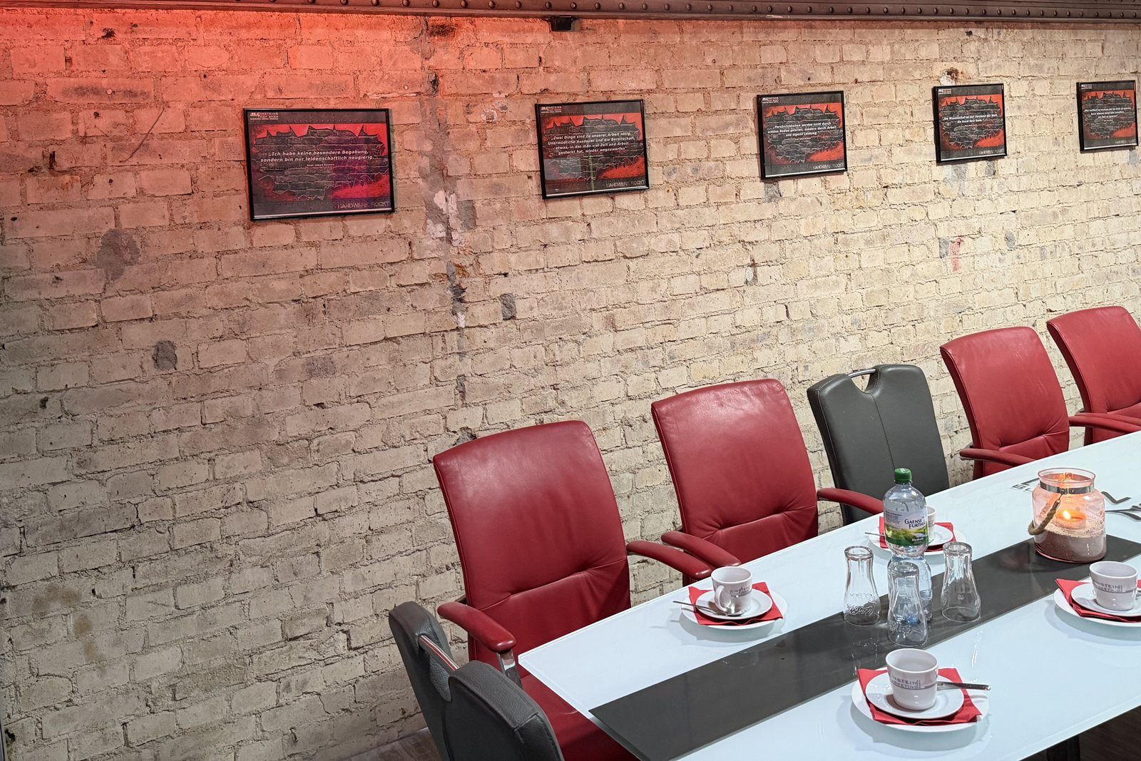 Tagungstisch mit roten Lederstühlen vor Backsteinwand